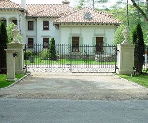 Custom wrought-iron gate design with concrete pillars, stone statues, and wrapped keypad post. Designed and installed by Tri State Gate, New York.