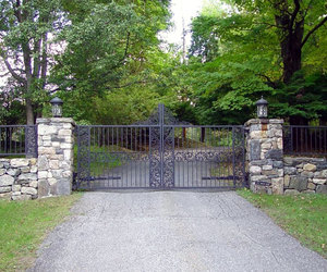 Ornate wrought-iron driveway gate with matching iron fencing. Designed and installed by Tri State Gate, New York.